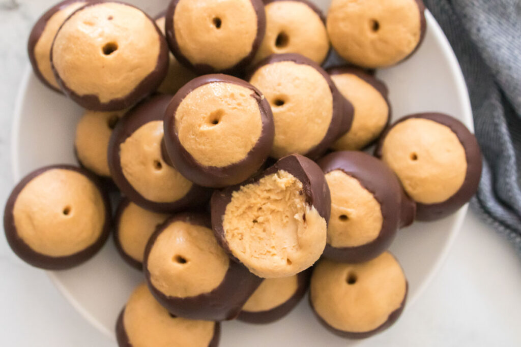 A plate of homemade buckeyes, those delightful peanut butter balls partially dipped in chocolate, with one showing a bite taken out.