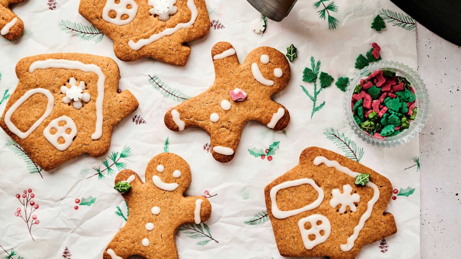 Air fryer gingerbread cookies shaped like houses and people rest on parchment paper, adorned with white icing and surrounded by small colorful candies.