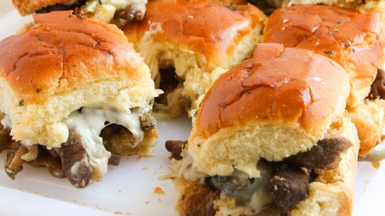 Close-up of Philly Cheesesteak sliders with melted cheese on a white surface.