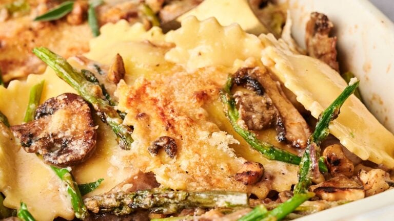 Close-up of a delectable ravioli casserole featuring tender mushrooms, crisp asparagus, and a golden, crispy cheese topping, all nestled in a baking dish.