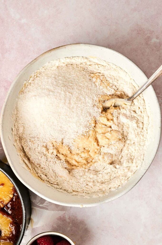Bowl with cake batter being mixed, topped with flour.