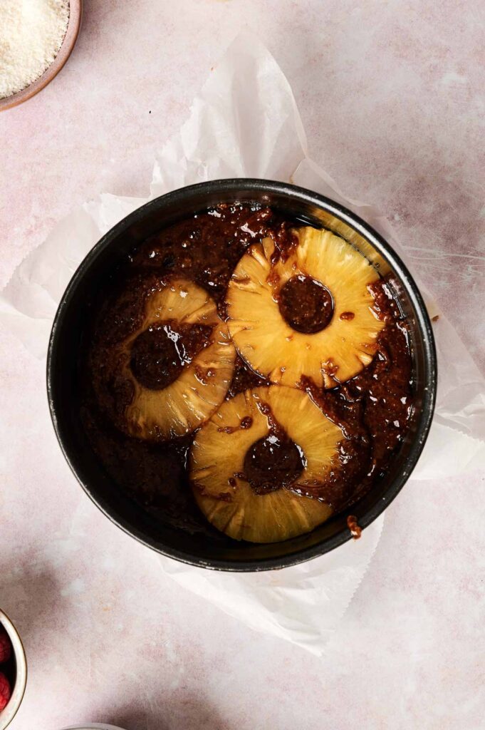 Top view of a round cake tin containing pineapple upside-down cake batter, with three pineapple rings sitting on top.