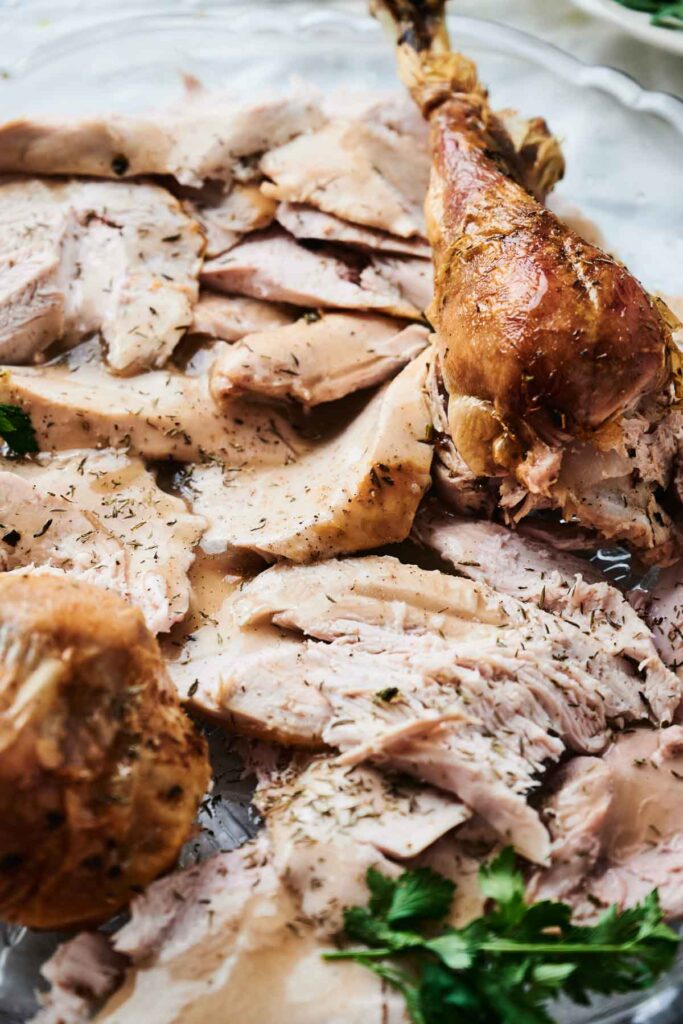 Slices of roasted turkey with herbs on a platter, garnished with fresh parsley.
