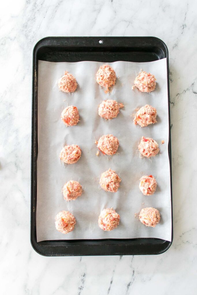 Raw cookie dough balls sit on a parchment-lined baking sheet, tempting as ever. Nearby, Rotel cream cheese sausage balls add a savory twist to the kitchen's aroma.