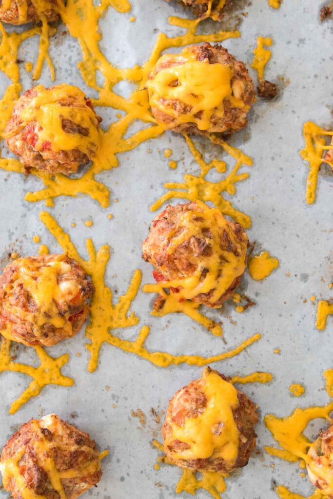 Baked meatballs topped with melted cheese and a hint of Rotel, all on a parchment-lined baking sheet.