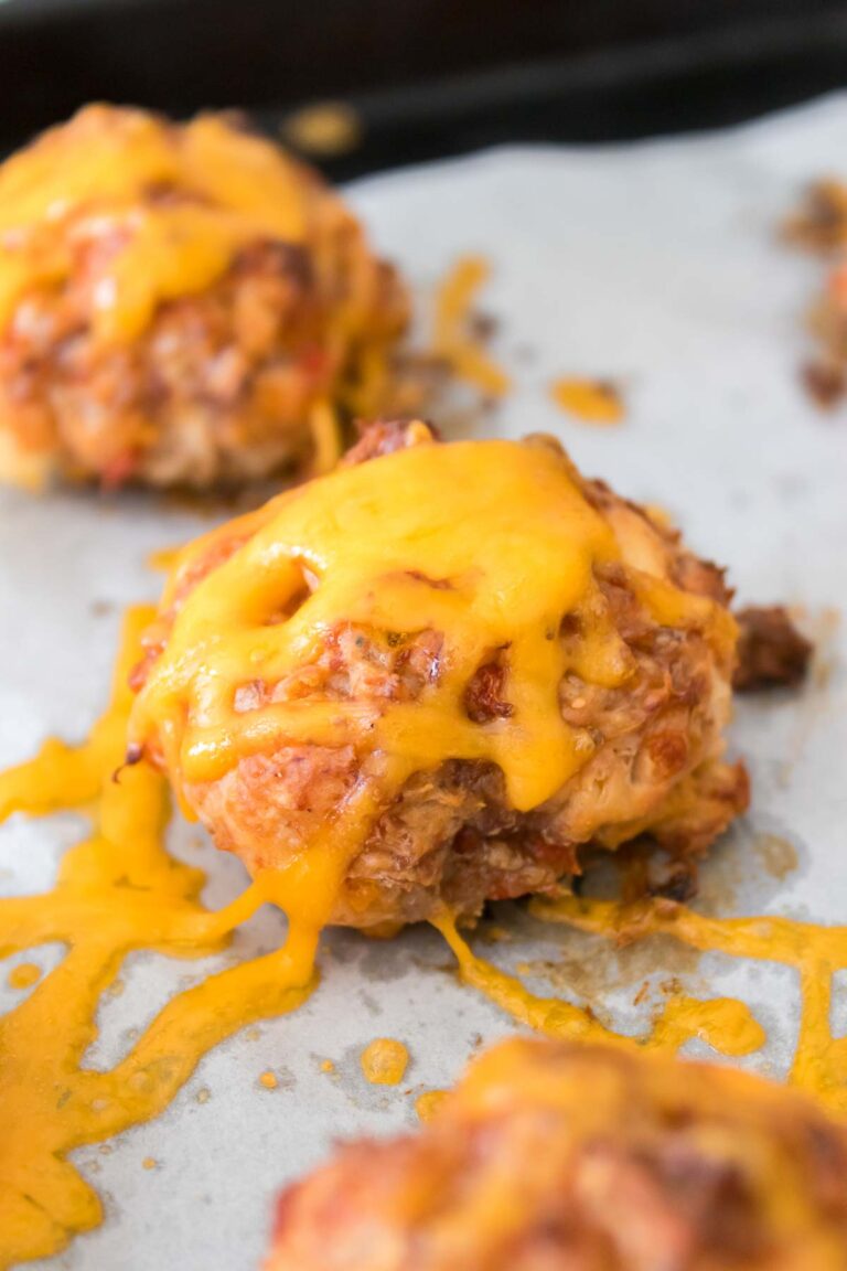 Baked meatballs topped with melted cheddar cheese on a parchment-lined tray, reminiscent of the savory Rotel cream cheese sausage balls.