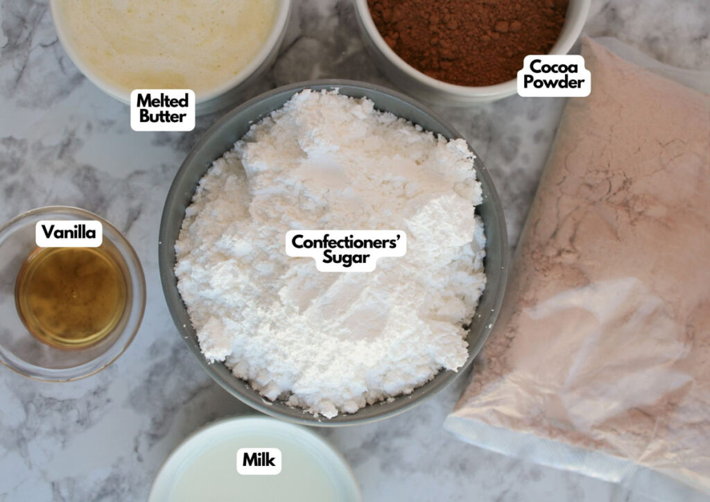 Ingredients for frosting displayed on a countertop: bowls of melted butter, vanilla, milk, cocoa powder, and a bowl and bag of confectioners&rsquo; sugar&mdash;perfect for making festive Rudolph cupcakes.