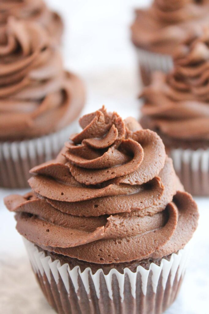 Four Rudolph cupcakes adorned with swirled chocolate frosting sit snugly in white paper liners, ready to delight any holiday gathering.