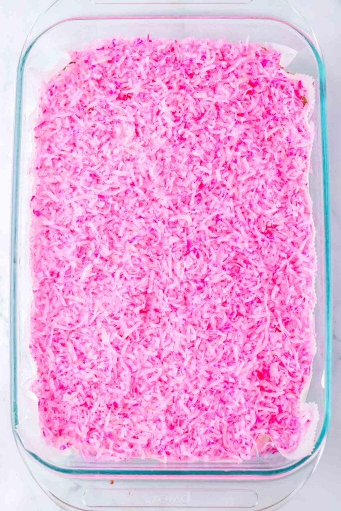 A rectangular glass dish holds pink-tinted shredded coconut, reminiscent of Pink Snoball Brownies, on a white surface.