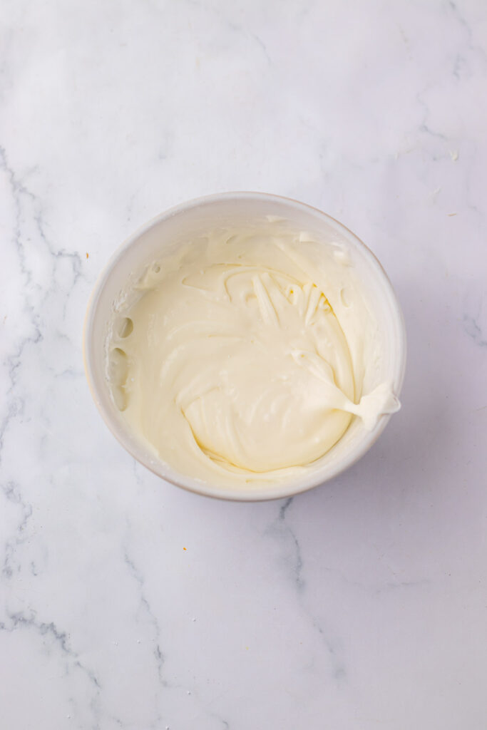 A bowl filled with smooth, creamy white batter, perfect for crafting a copycat Starbucks Red Velvet Loaf, rests on a marble surface.