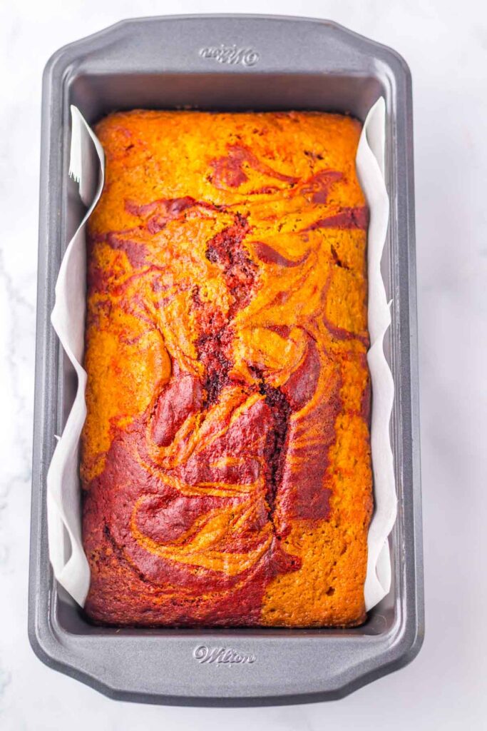 A copycat Starbucks Red Velvet Loaf sits elegantly in a rectangular baking pan on a pristine white surface, showcasing its vibrant swirls.