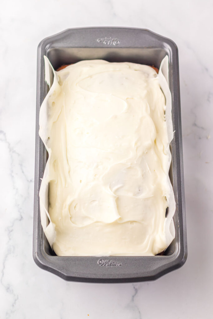 A baking pan holds a copycat Starbucks red velvet loaf covered in white icing, resting elegantly on a marble countertop.