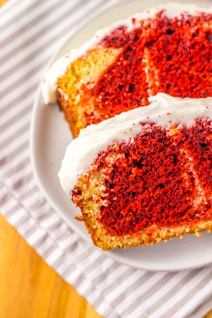 Two slices of copycat Starbucks red velvet marble cake with frosting, served on a white plate over a striped cloth.