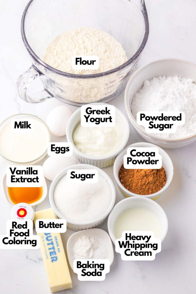 Ingredients on a counter include flour, powdered sugar, Greek yogurt, cocoa powder, heavy whipping cream, baking soda, butter, sugar, vanilla extract, milk, eggs, and red food coloring—everything needed to create a copycat Starbucks Red Velvet Loaf.