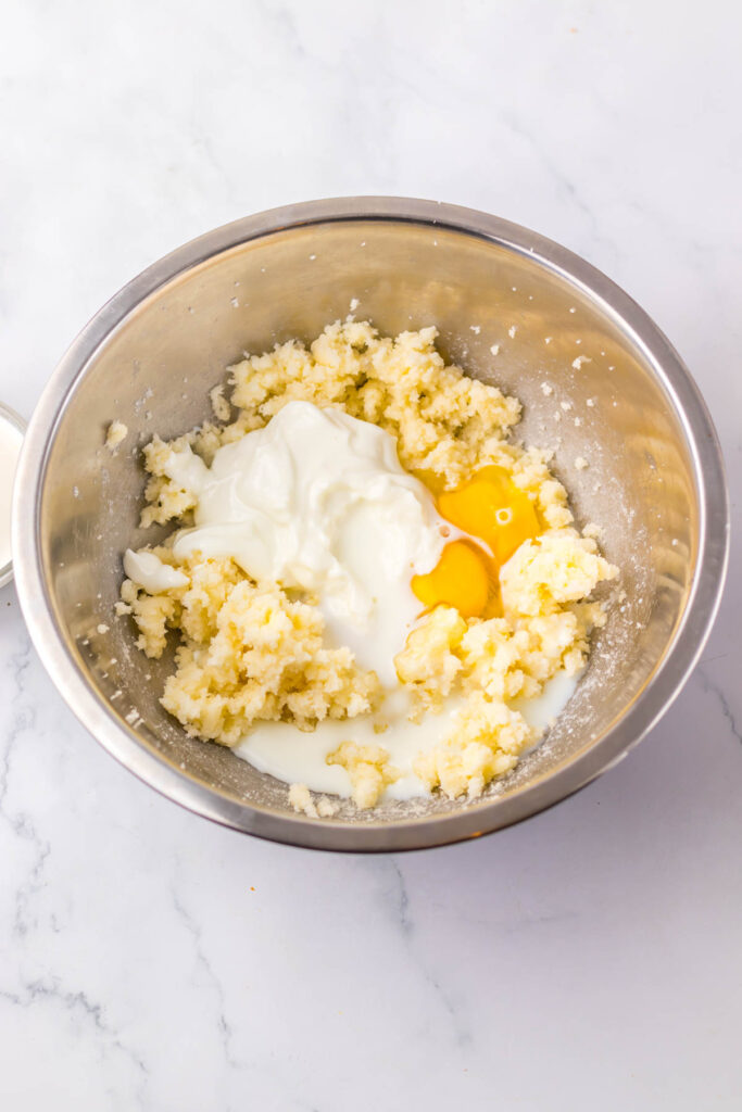A mixing bowl on a white marble surface holds the creamed butter and sugar, an egg, and yogurt—the first steps in crafting a copycat Starbucks Red Velvet Loaf.