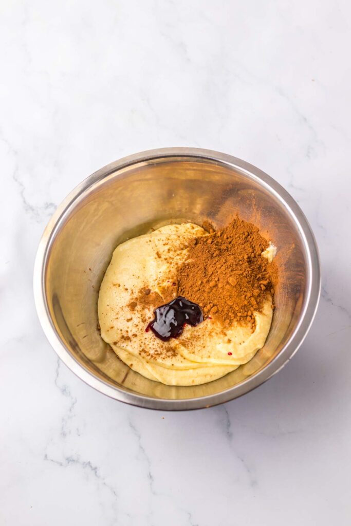 A metal bowl containing dough, with brown spices and a dark liquid topping it, sits on a white marble surface, reminiscent of preparing a copycat Starbucks Red Velvet Loaf.