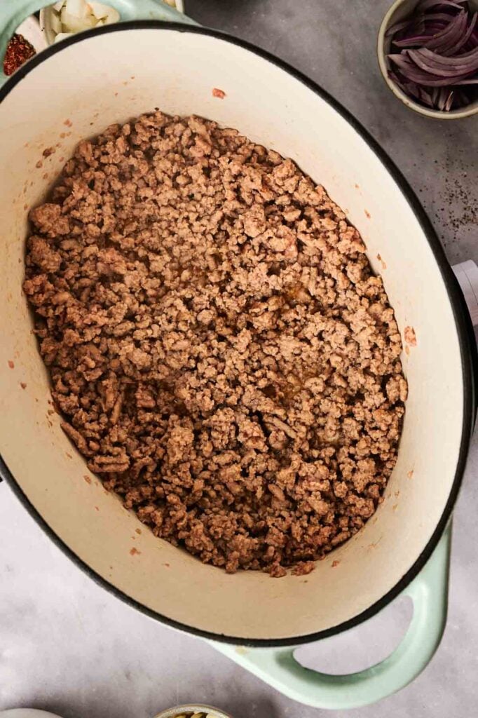 A large pot of taco soup, brimming with cooked ground beef, sits on the kitchen counter surrounded by small bowls of vibrant ingredients.