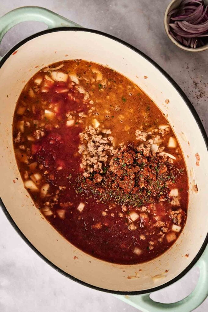 A large pot filled with a simmering mixture that suggests the savory essence of taco soup, complete with ground meat, diced onions, tomatoes, and spices. A small bowl with sliced onions adds to the scene in the background.