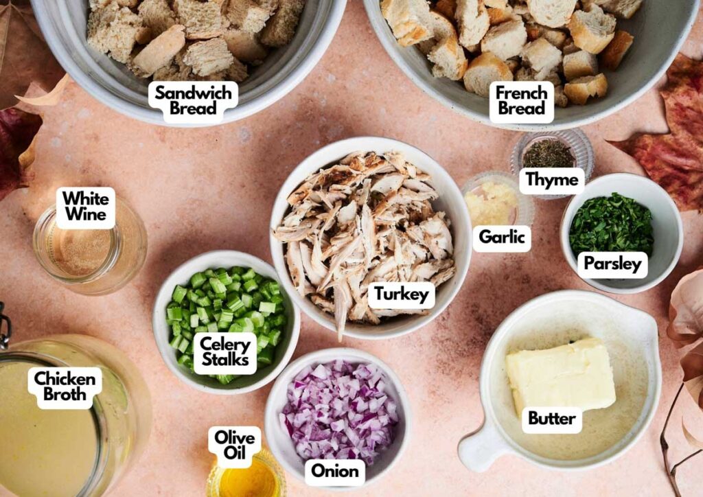 Ingredients for a Thanksgiving casserole stuffing are laid out in bowls, including turkey, French bread, sandwich bread, onion, celery, white wine, chicken broth, olive oil, butter, garlic, parsley, and thyme.
