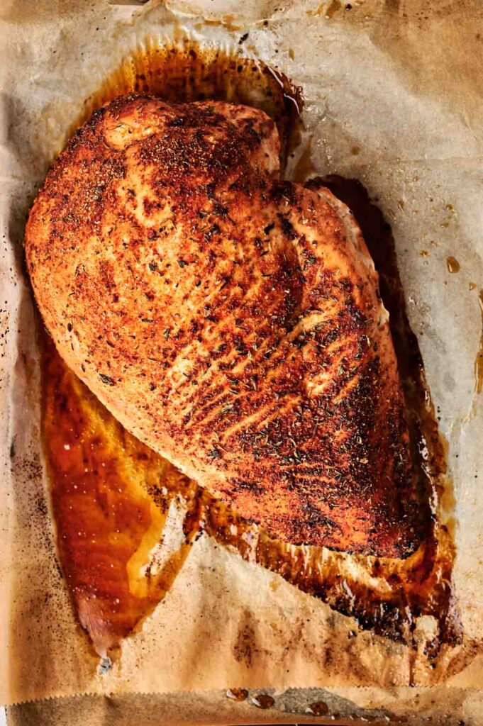 Roasted seasoned chicken breast on a sheet of parchment paper with visible juices.