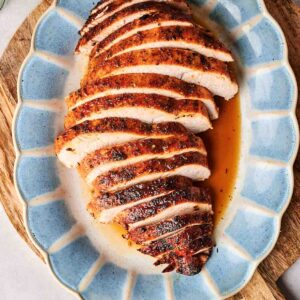 Sliced roasted turkey breast on a blue oval platter, with juices.