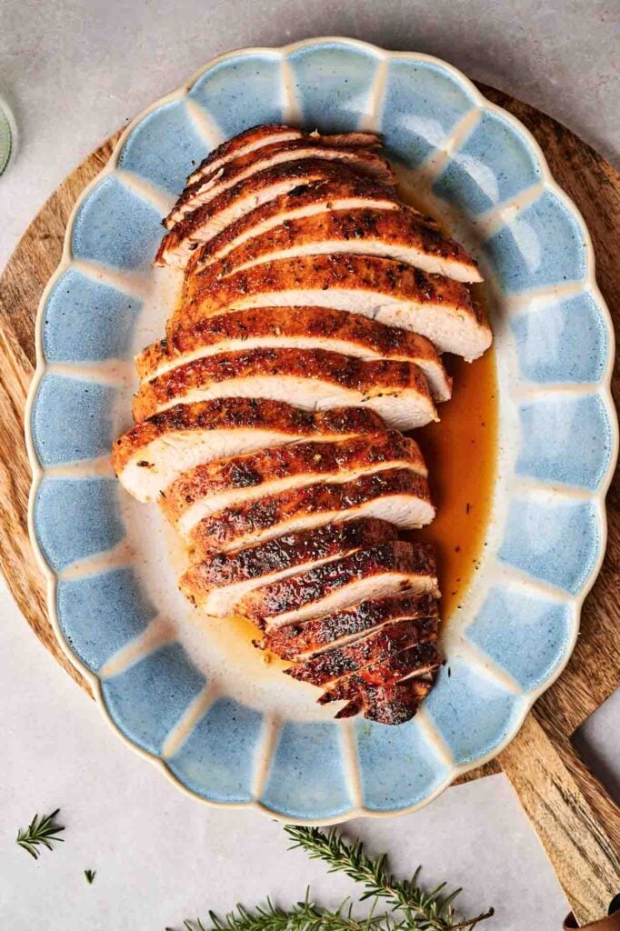 Sliced roasted turkey breast on a blue oval platter, with juices.