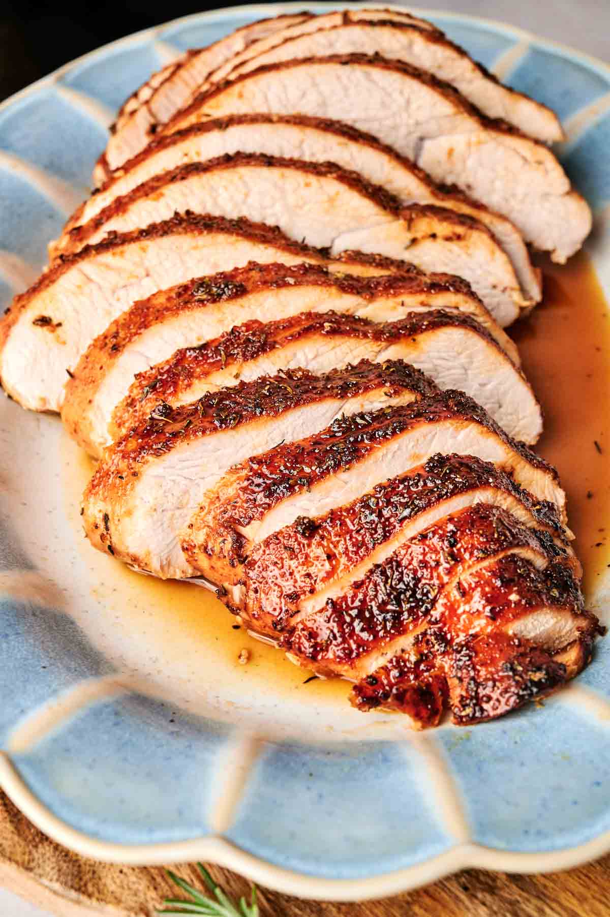 Sliced roasted turkey breast on a blue plate with juices.