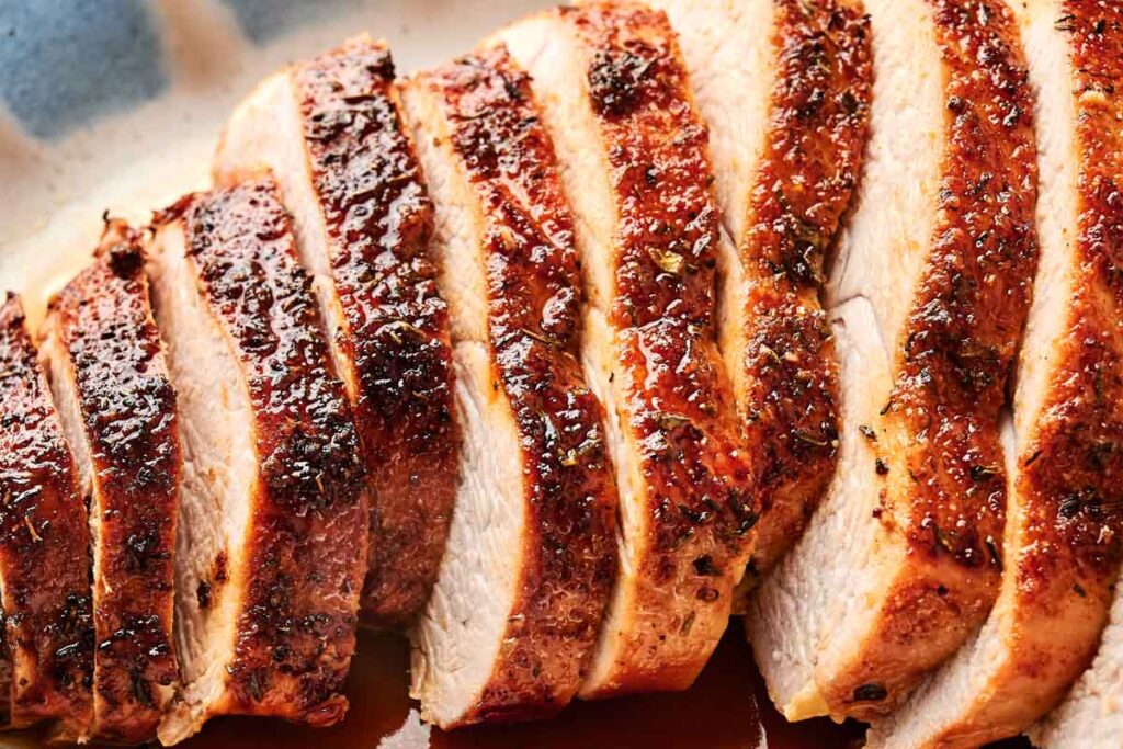 Sliced cooked turkey breast with a golden brown, crispy skin on a platter.