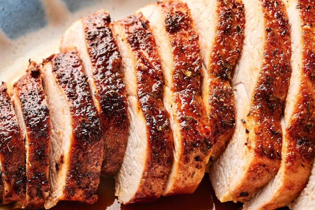 Sliced, roasted turkey breast with seasoned, crispy skin arranged on a serving platter.