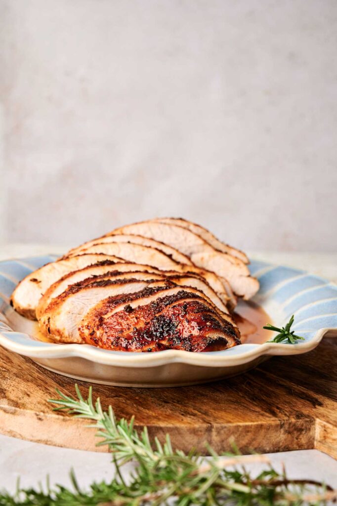 Slices of roasted turkey breast on a scalloped plate, garnished with sprigs of rosemary.