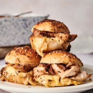 Three turkey sliders with melted cheese on seeded buns are stacked on a white plate.