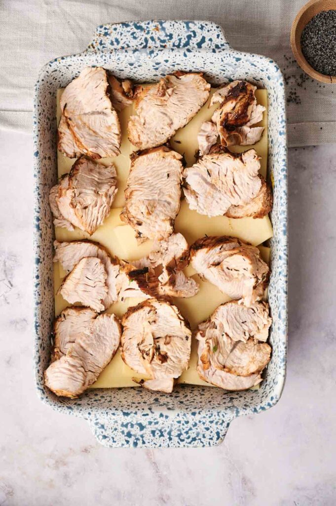 Sliced cooked meat on top of sliced potatoes in a speckled baking dish, reminiscent of deconstructed turkey sliders.