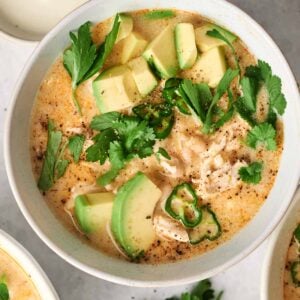 Bowl of creamy white chicken chili topped with avocado slices, cilantro, parsley, and green chili, served with a side of sour cream—perfect for those who love the flavors of an air fryer twist.