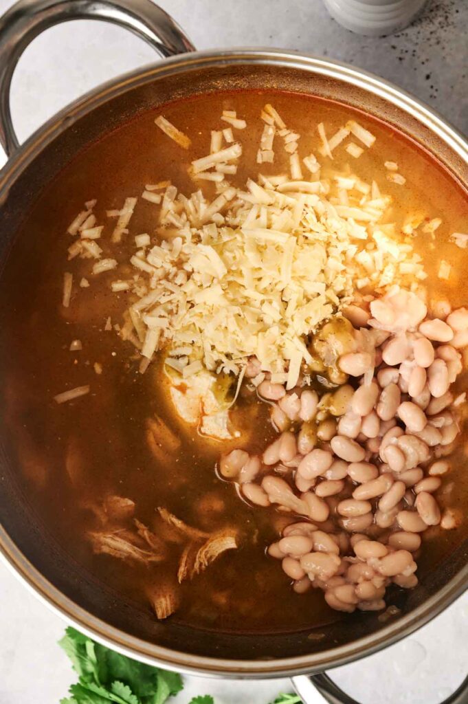 A hearty white chicken chili features a soup pot brimming with shredded chicken, white beans, and green chilies, topped with a sprinkle of grated cheese.