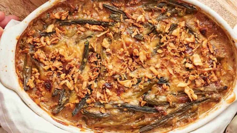 A baked dish of green bean casserole topped with crispy fried onions in a white oval baking dish.