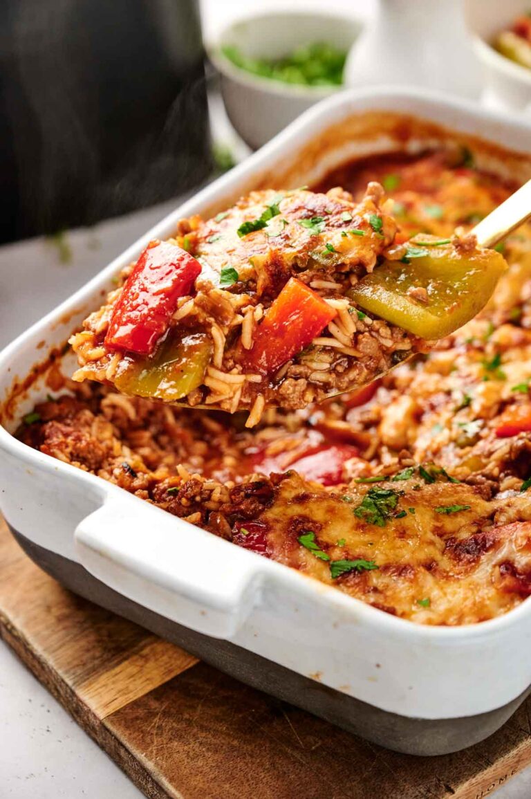 A serving of Air Fryer Stuffed Pepper Casserole with rice, bell peppers, and melted cheese is being lifted from a white baking dish.