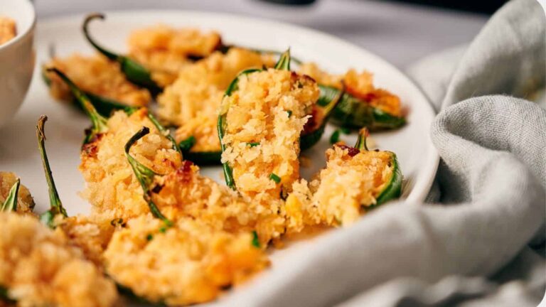 A plate of baked stuffed jalapeños topped with golden breadcrumbs.