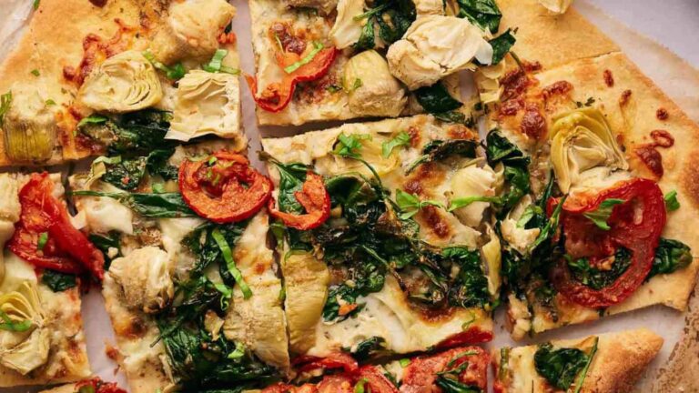 Close-up of a sliced pizza with artichokes, spinach, tomatoes, and cheese on a thin crust.