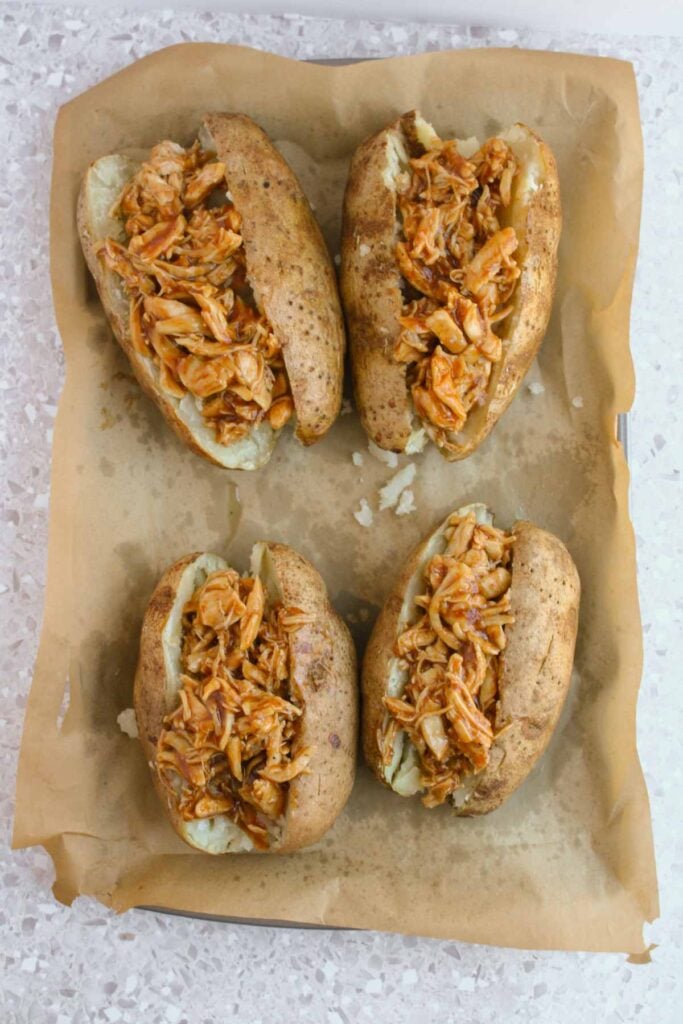 Four BBQ chicken stuffed potatoes rest on parchment paper, each brimming with tender, shredded barbecue chicken.