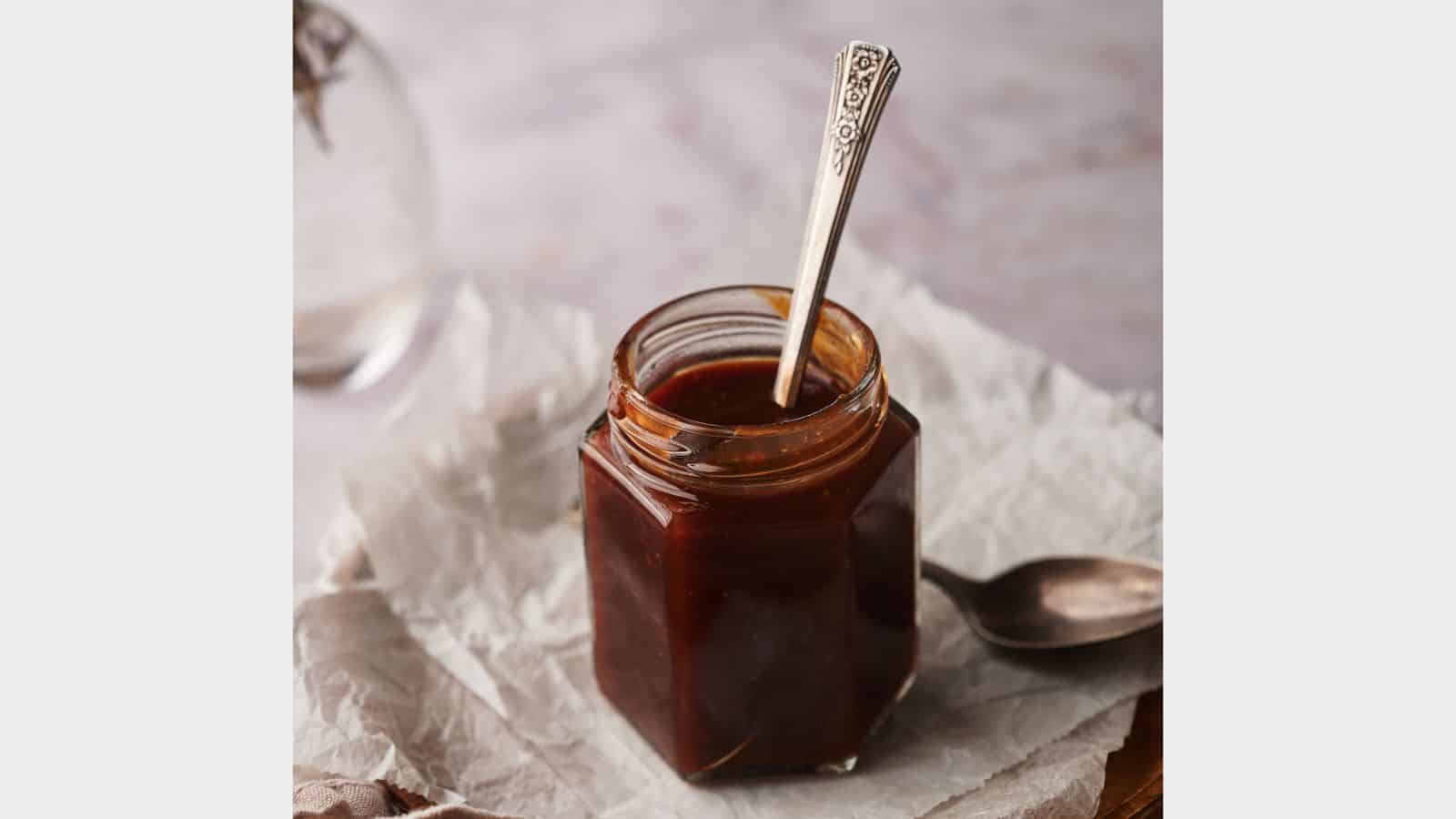 Homemade BBQ sauce in a jar with two spoons by the side.