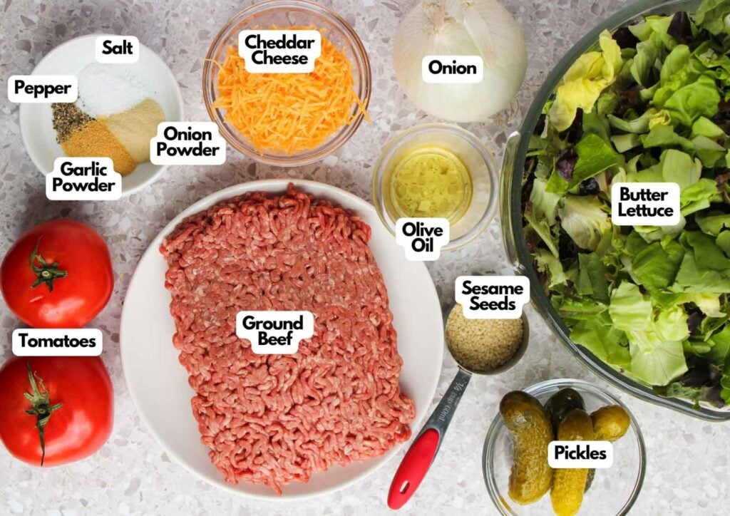 Various labeled ingredients for a Big Mac Salad, including ground beef, cheddar cheese, lettuce, tomatoes, onion, pickles, olive oil, sesame seeds, and assorted seasonings.