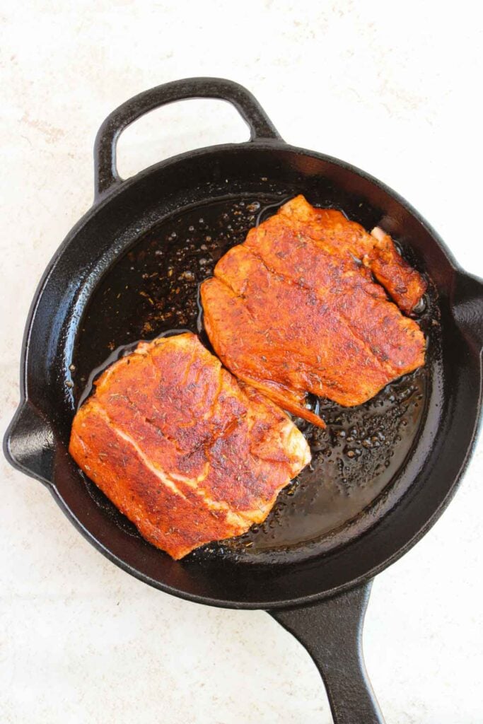 Two seasoned steaks cooking in a black cast iron skillet.