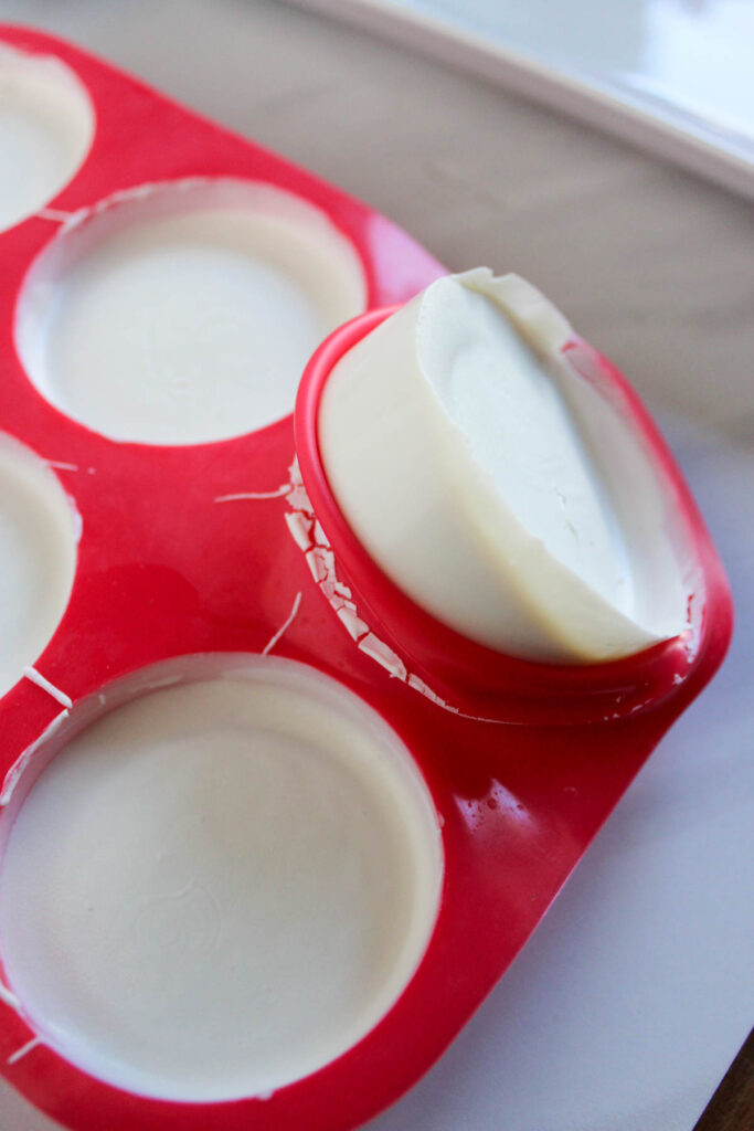 Round white soap bars in a red silicone mold, with one bar partially removed.