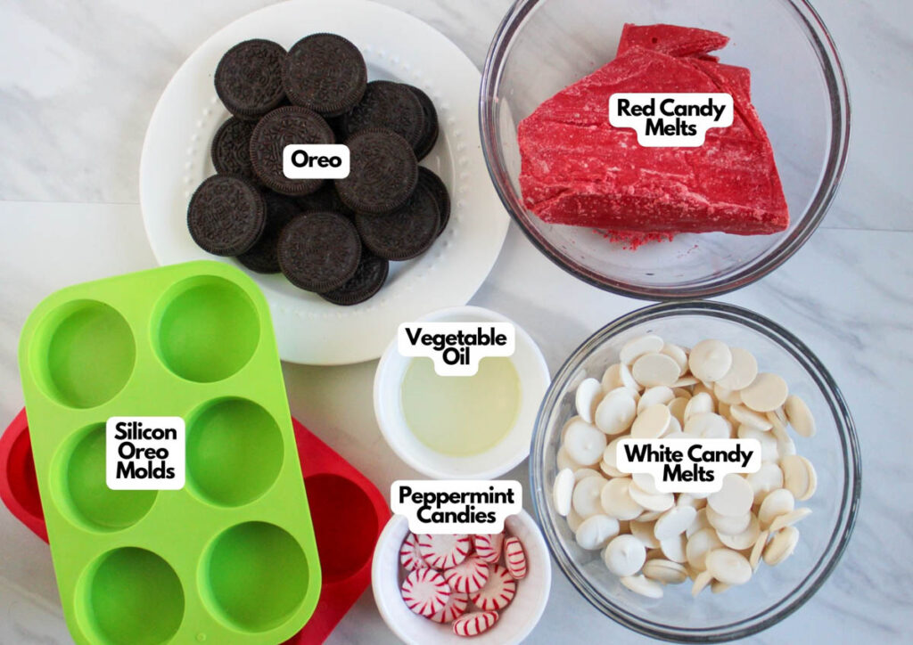 Ingredients and tools for candy cane Oreos: Oreo cookies, red and white candy melts, vegetable oil, peppermint candies, and silicone Oreo molds displayed on a countertop.
