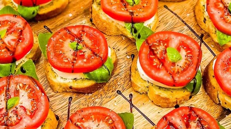 Slices of toasted bread topped with fresh basil, mozzarella, and tomato, drizzled with balsamic glaze on a wooden board.