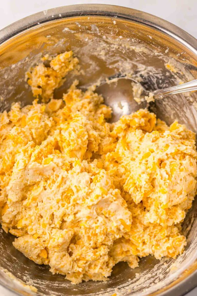 A mixing bowl filled with a cheese and dough mixture, hinting at the delightful aroma of cheddar bay biscuits, with a spoon partially submerged.