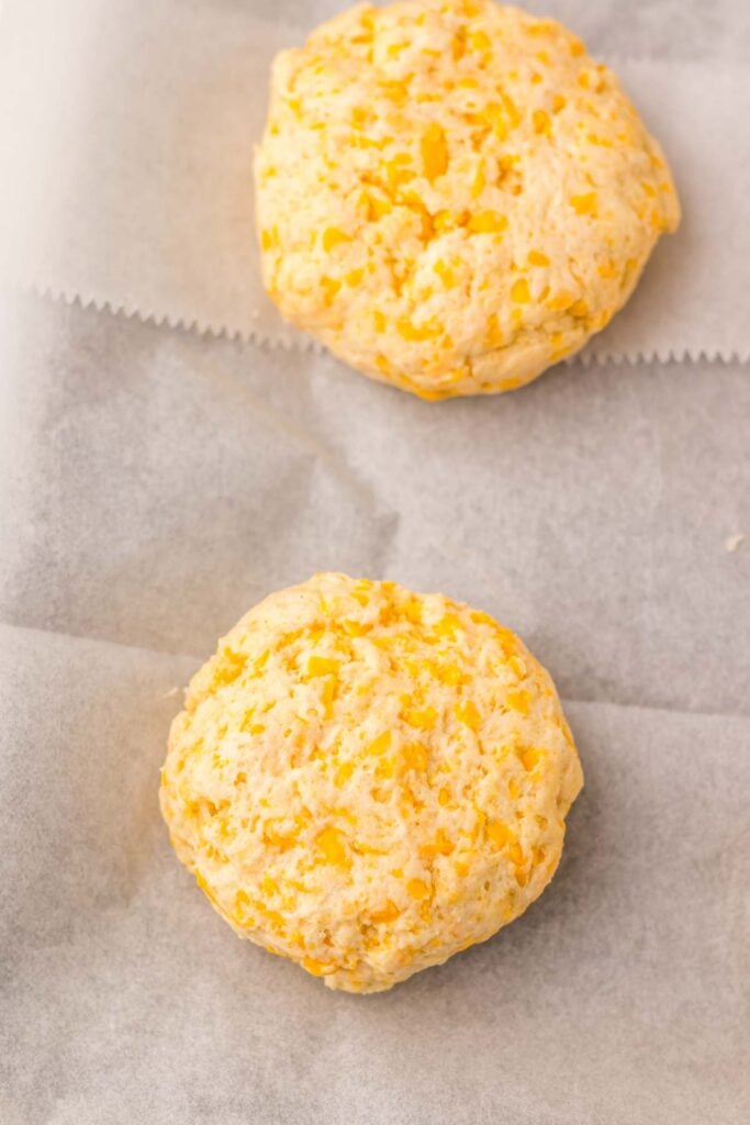 Two cheddar bay biscuits rest on parchment paper, their cheesy aroma filling the air.