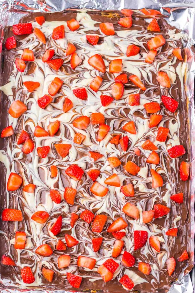 A tray of chocolate-covered strawberry toffee bark features marbled dark chocolate swirls, topped with chopped strawberries.