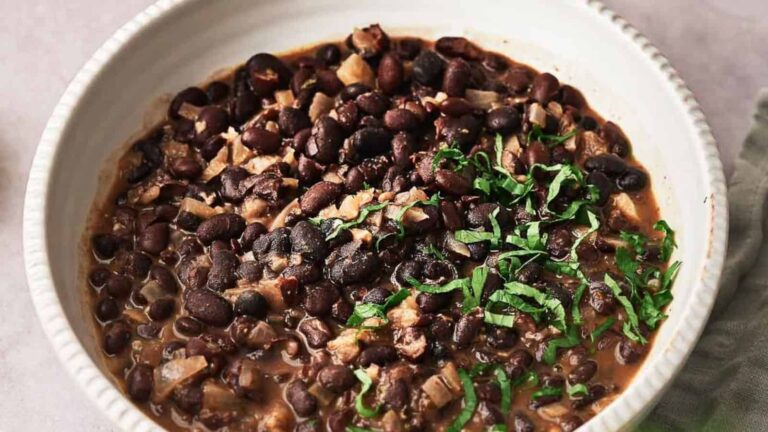 A bowl of cooked black beans topped with chopped greens.