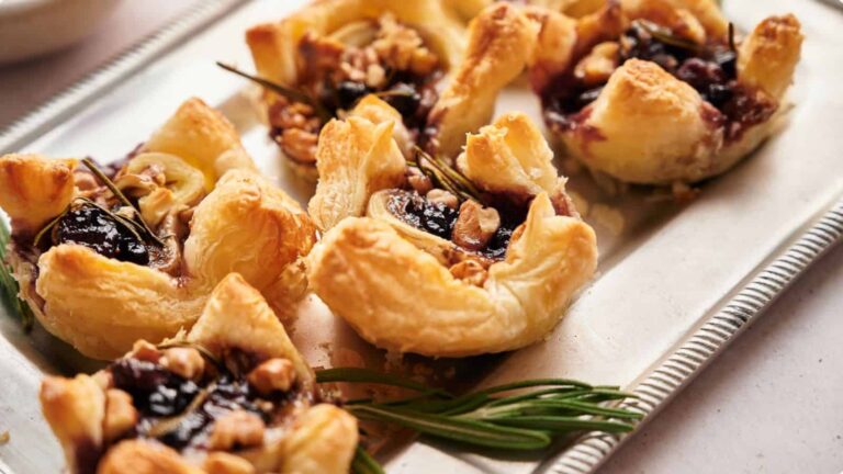 Puff pastry tarts with dark fruit filling, topped with walnuts and rosemary, on a silver tray.